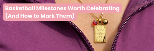 Gold Home Court basketball necklace with basketball court pendant, basketball charm and red heart gem charm worn with a purple athletic jacket, featured in an article about celebrating basketball milestones.