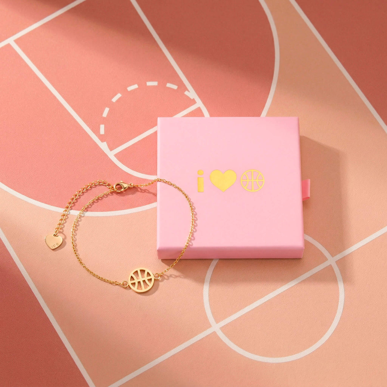 Gold basketball bracelet displayed beside an I Heart Hoops gift box on a pink basketball court background