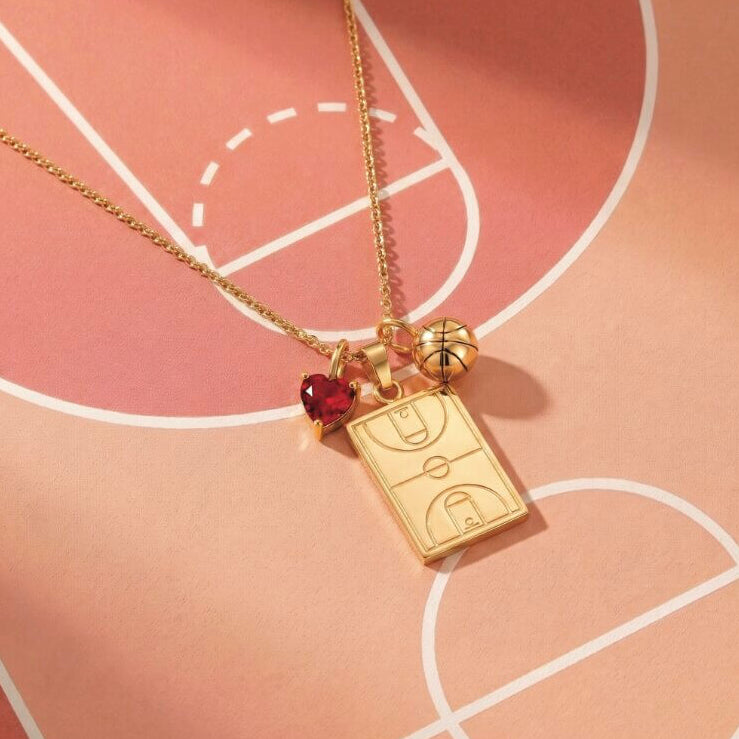 Home Court basketball necklace featuring a basketball court pendant, basketball charm and red heart-shaped gem charm on a pink basketball court background