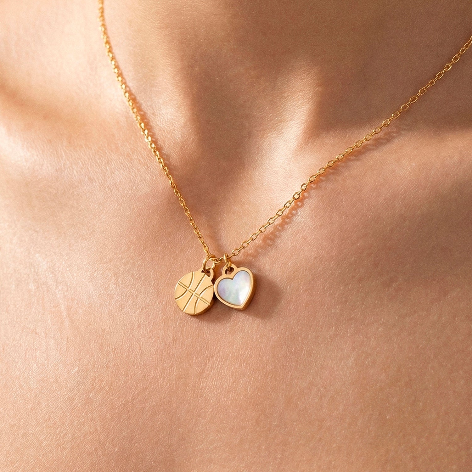 Close-up of gold necklace with basketball and pearl heart pendant worn on neck